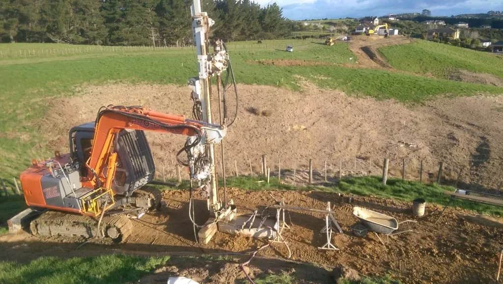 Bored-pile drilling rig working a paddock at the Ormiston Road subdivision, Flat Bush, Auckland, with new housing on the ridge behind