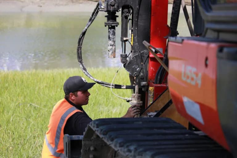 Explore Geotechnical crew member setting up a cone penetration test beside a river, working off the rig tracks