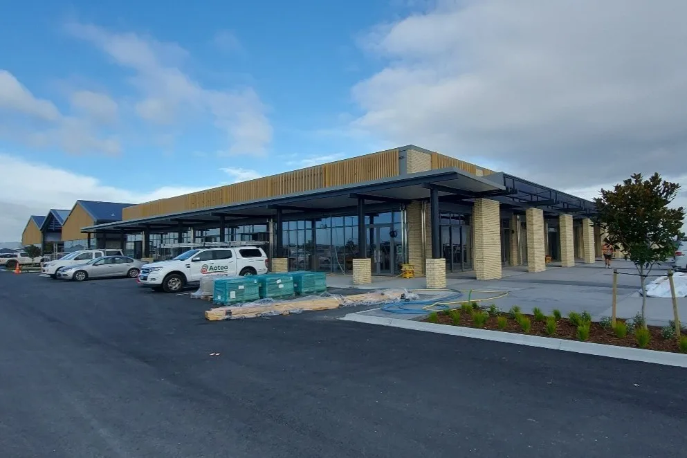 Newly completed commercial building in Papamoa with a timber-battened facade, brick columns, glazed shopfronts and a covered walkway